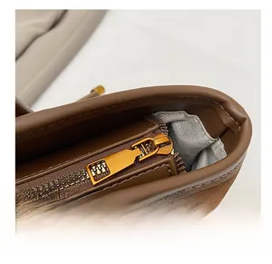 Detail view of smooth golden metal zipper and herringbone fabric lining on a brown bag