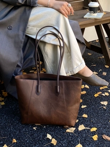 Detail of dark brown matte leather tote bag in an autumn outdoor lifestyle setting