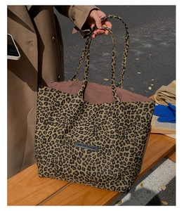 Outdoor view of a leopard print tote bag with black leather label on a wooden bench