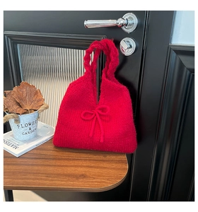 Macro shot of red knitted tote bag with bow detail and braided strap on wooden background