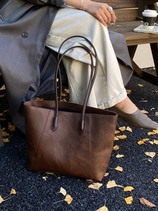 Detailed view of brown matte leather tote bag handle and stitching in an autumn park setting