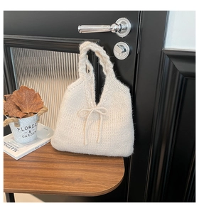Detailed knit texture of white knitted handbag featuring elegant bow on a wooden table