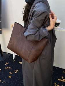 Dark brown leather tote bag with large capacity shown on shoulder of a model in stylish outfit