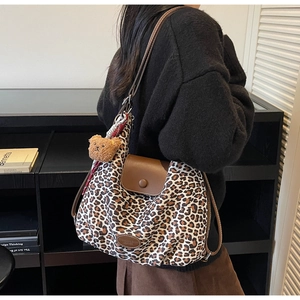 Detail of leopard print tote bag featuring a leather flap and a plush bear pendant charm