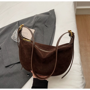 Detail view of dark brown suede crescent bag with leather strap on grey blazer