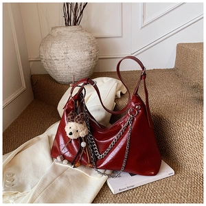 Detail of dark red vintage leather handbag with silver chain and cute teddy bear charm