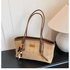 Detailed close-up of brown suede tote bag with diamond quilting and beaded charm