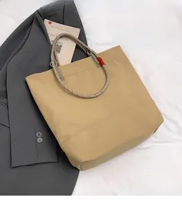 Detail view of khaki nylon tote bag featuring durable dual-tone rope handles and red accent