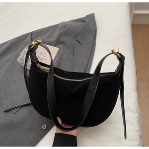 Detail of a black suede crescent bag on a grey blazer with gold metal hardware and zipper