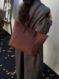 Detail view of large reddish-brown suede tote bag worn by model in autumn scenery