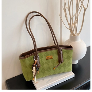 Detail of green quilted tote bag with brown handles and bead charm beside a book