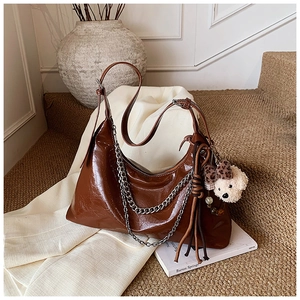 Detail of glossy brown hobo bag featuring silver chain, leather tassels and a bear charm