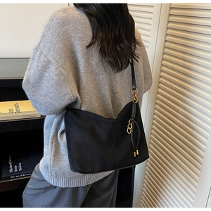 Detailed view of a black suede hobo bag with gold chain and knot tassel on a model