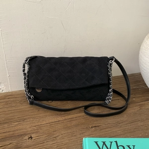 Close-up of black quilted suede shoulder bag with silver chain strap on wood