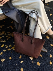 Detailed close-up of brown suede tote bag with long straps in an autumn street setting