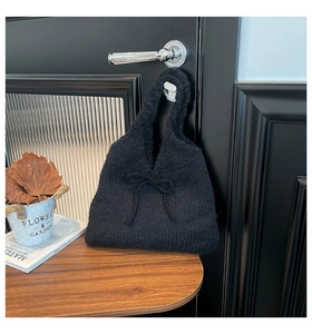 Detail of black knit tote bag with bow accent hanging on a handle in home setting