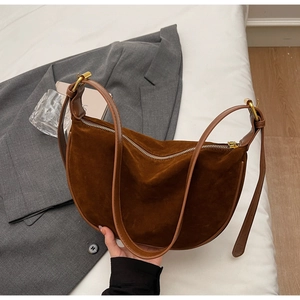 Close-up of brown suede hobo bag with adjustable strap held against a grey blazer