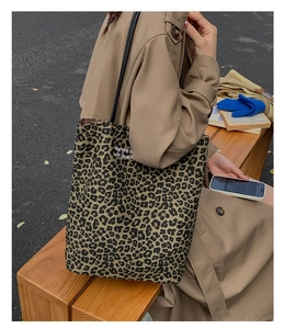 Detail of leopard print canvas tote bag with black strap worn by model on bench