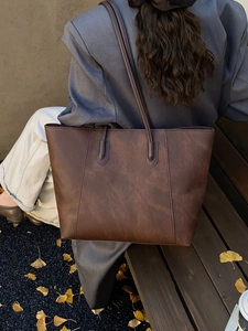 Detail of a large dark brown tote bag in vintage faux leather on a model's shoulder