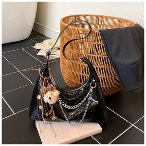 Detail of glossy black patent leather crescent bag with silver chains and bear charm