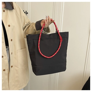 Detail of black tote bag featuring thick red and yellow braided rope handles with leather grip
