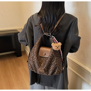 Detail of leopard print canvas tote bag featuring brown leather flap and bear charm accessory