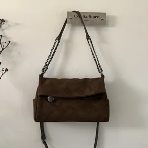 Detail of dark brown quilted suede texture and silver metal chain strap on shoulder bag