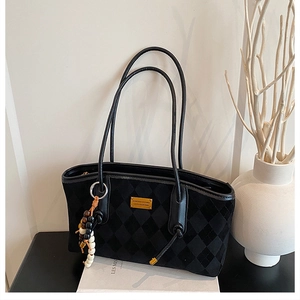 Close-up of black suede tote bag with golden logo plate and colorful beaded charm strap