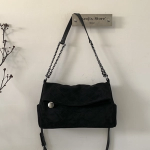 Detail of a black quilted suede shoulder bag with silver chain and metal clasp