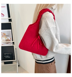 Close-up of a red knitted shoulder bag with bow detail on a model in a minimalist room