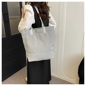 Close-up of gray tote bag with woven shoulder strap and red label detail on back