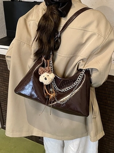 Deep brown glossy chain handbag with plush bear charm worn with a stylish trench coat