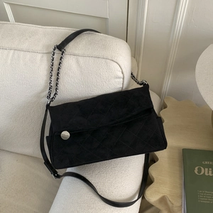 Detail shot of black suede quilted shoulder bag with silver chain on white sofa