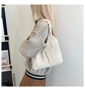 Close-up of cream knit tote bag with bow detail and woven strap on model's shoulder