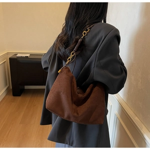 Detail of dark brown suede hobo bag featuring a gold chain and leather woven strap