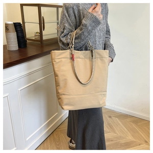 Detail of minimalist khaki tote bag featuring knotted handles and red label accent