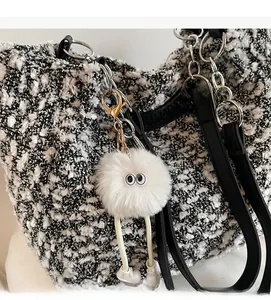 Close-up of a white fluffy monster charm with large eyes on a tweed handbag
