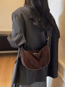 Deep brown suede crescent bag with leather strap shown in a stylish shoulder-carry style