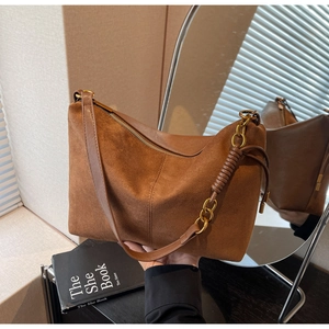 Detail view of brown suede shoulder bag with wide strap and decorative gold metal chain