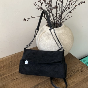 Close-up of black suede shoulder bag with quilted diamond pattern and silver chain strap