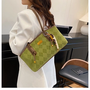 Detail of green checkerboard tote bag with brown leather handles and bead charm