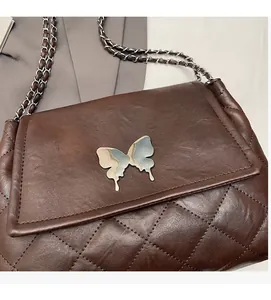 Détail d'un sac matelassé marron foncé avec fermoir papillon bleu argenté et bandoulière
