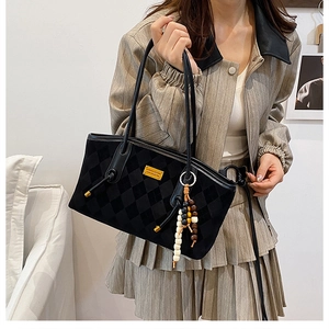 Detailed view of black suede tote bag featuring diamond quilt pattern and ethnic bead charm