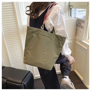 Detail of olive green canvas tote bag with colorful braided rope strap on model shoulder