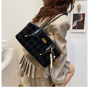 Detail of black quilted suede shoulder bag featuring gold hardware and beaded tassel