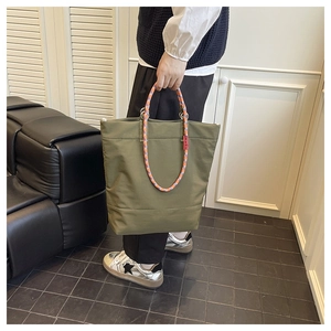 Close-up of army green tote bag with orange and purple braided rope handles and red tag