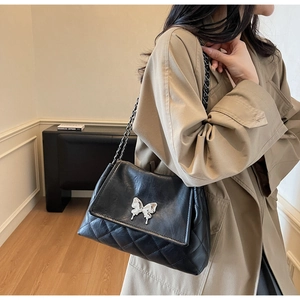 Détail d'un sac bandoulière noir matelassé avec fermoir papillon argenté et chaîne