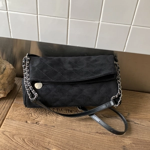Close-up of black quilted suede shoulder bag with silver chain and metal clasp