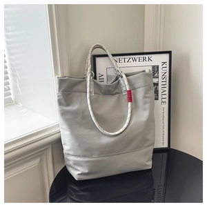Detail of grey tote bag showing woven rope handles and a small red decorative tag