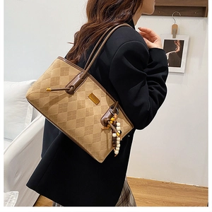 Close-up of diamond-quilted brown suede tote bag featuring a beaded tassel and gold logo